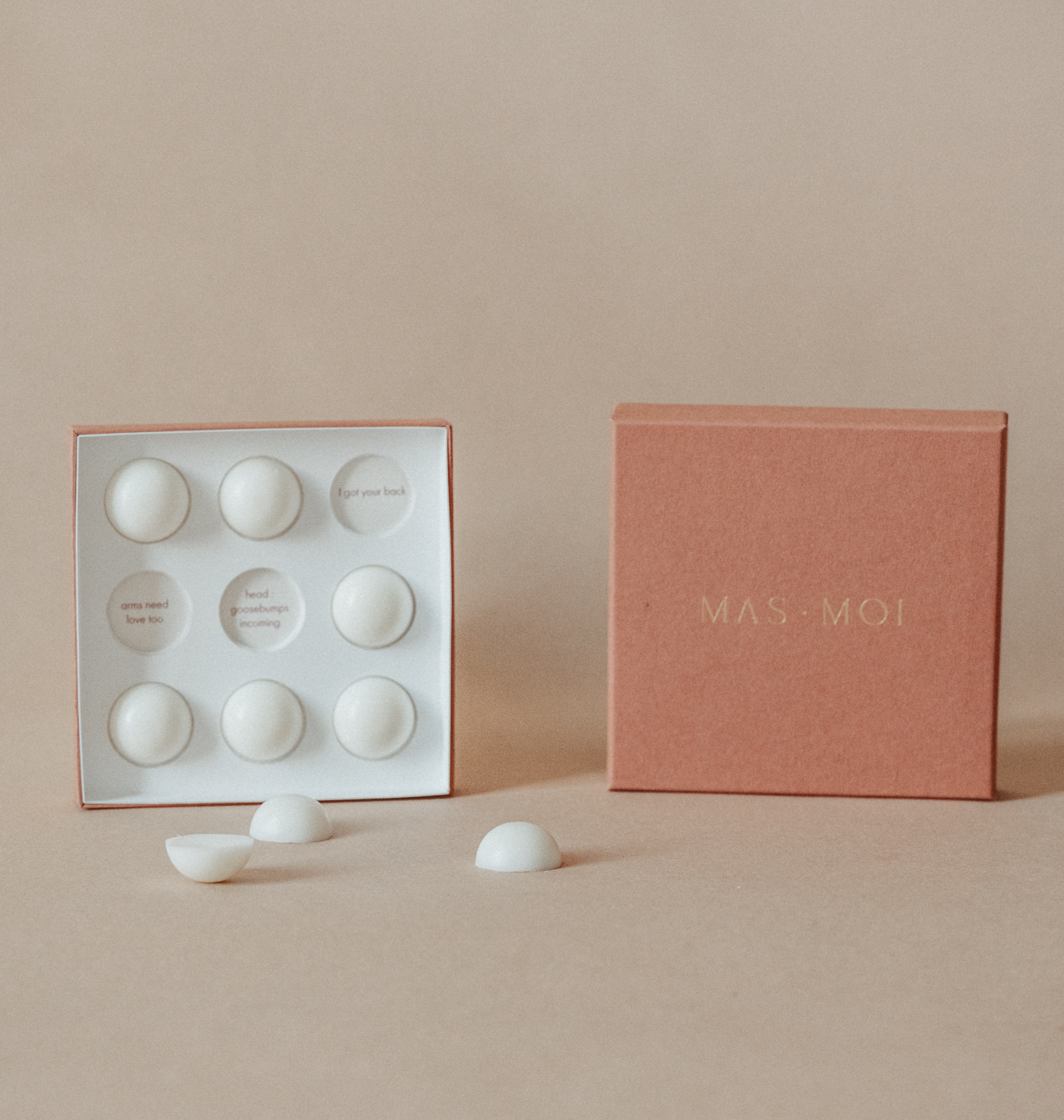 An open masmoi box revealing floral scent massage oil pearls inside, each designed to melt into nourishing oil for a soothing massage. The inner packaging includes playful text such as 'I got your back' and 'head goosebumps incoming,' adding a personalised touch. Set against a warm beige background, this luxurious product is perfect for a massage workshop or self-care ritual.