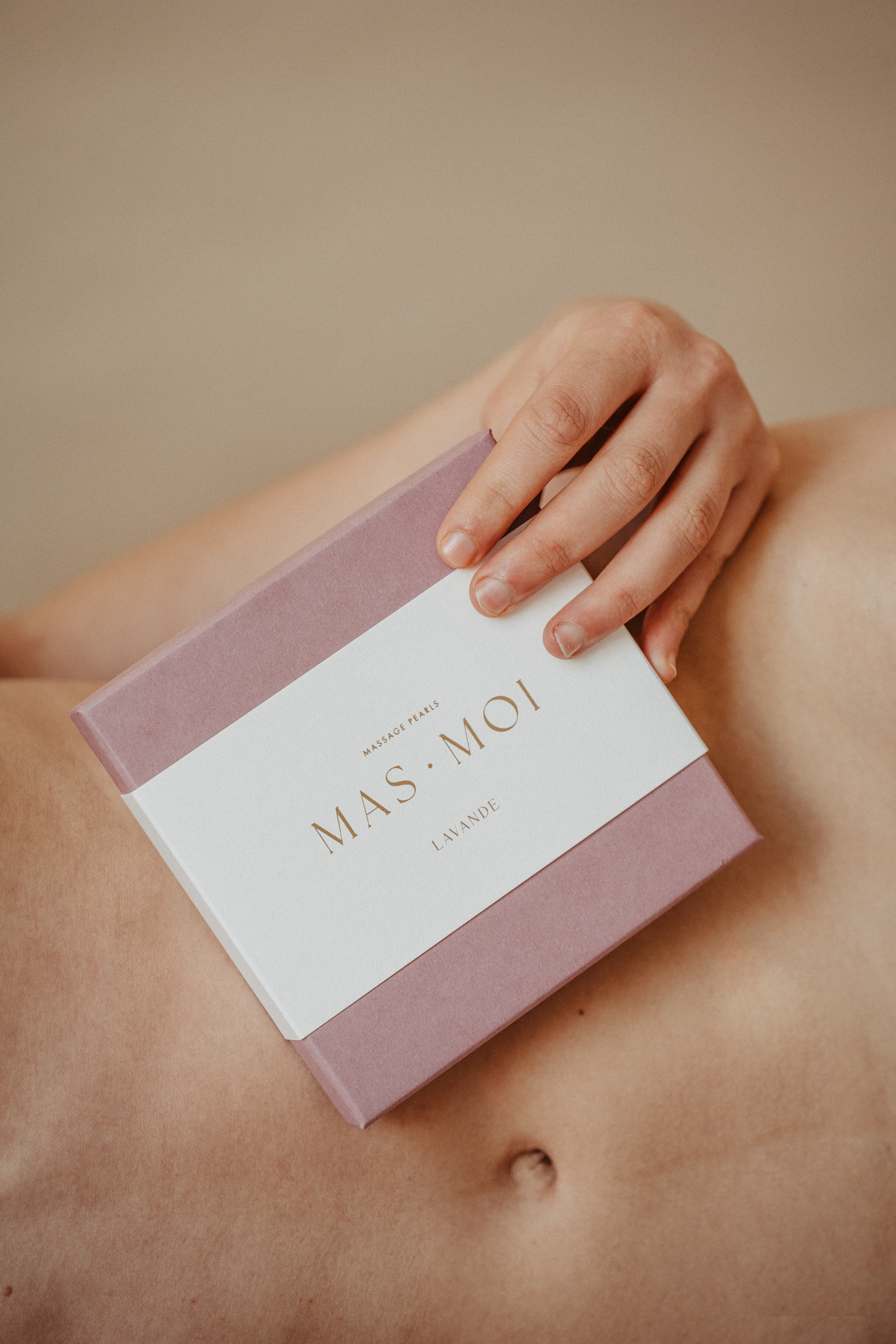 A person holds a Masmoi box labeled 'Lavande' against their bare torso, highlighting the Lavender Scent Massage Oil pearls inside. 