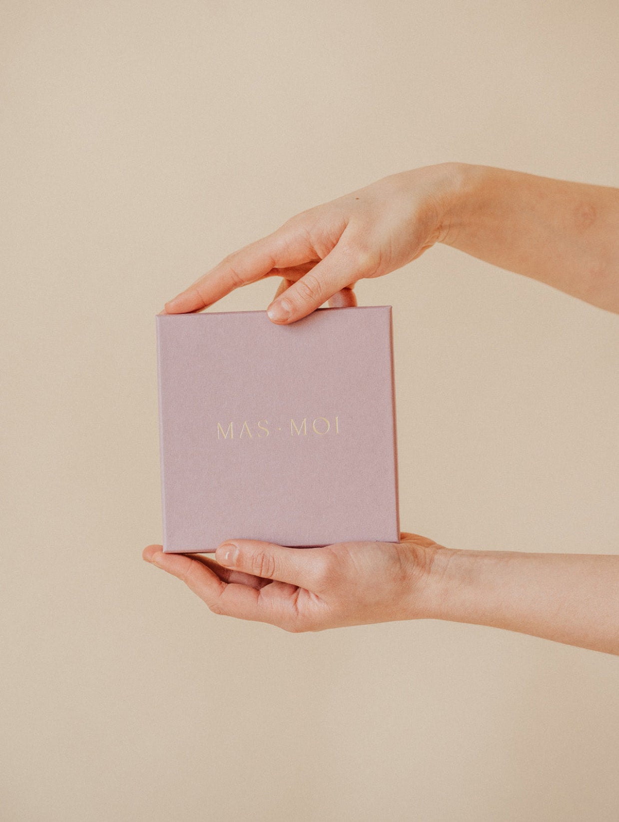 A pair of hands holding a masmoi box of lavender massage oil pearls. The minimalist packaging is a premium self-care product.